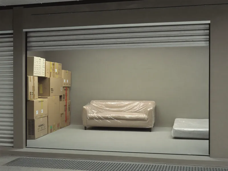 Climate-controlled storage unit holding a wrapped sofa, labelled boxes and a covered mattress